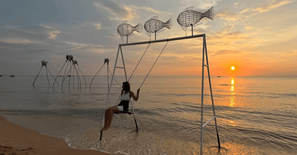 A woman on a swing on the beach at sunset